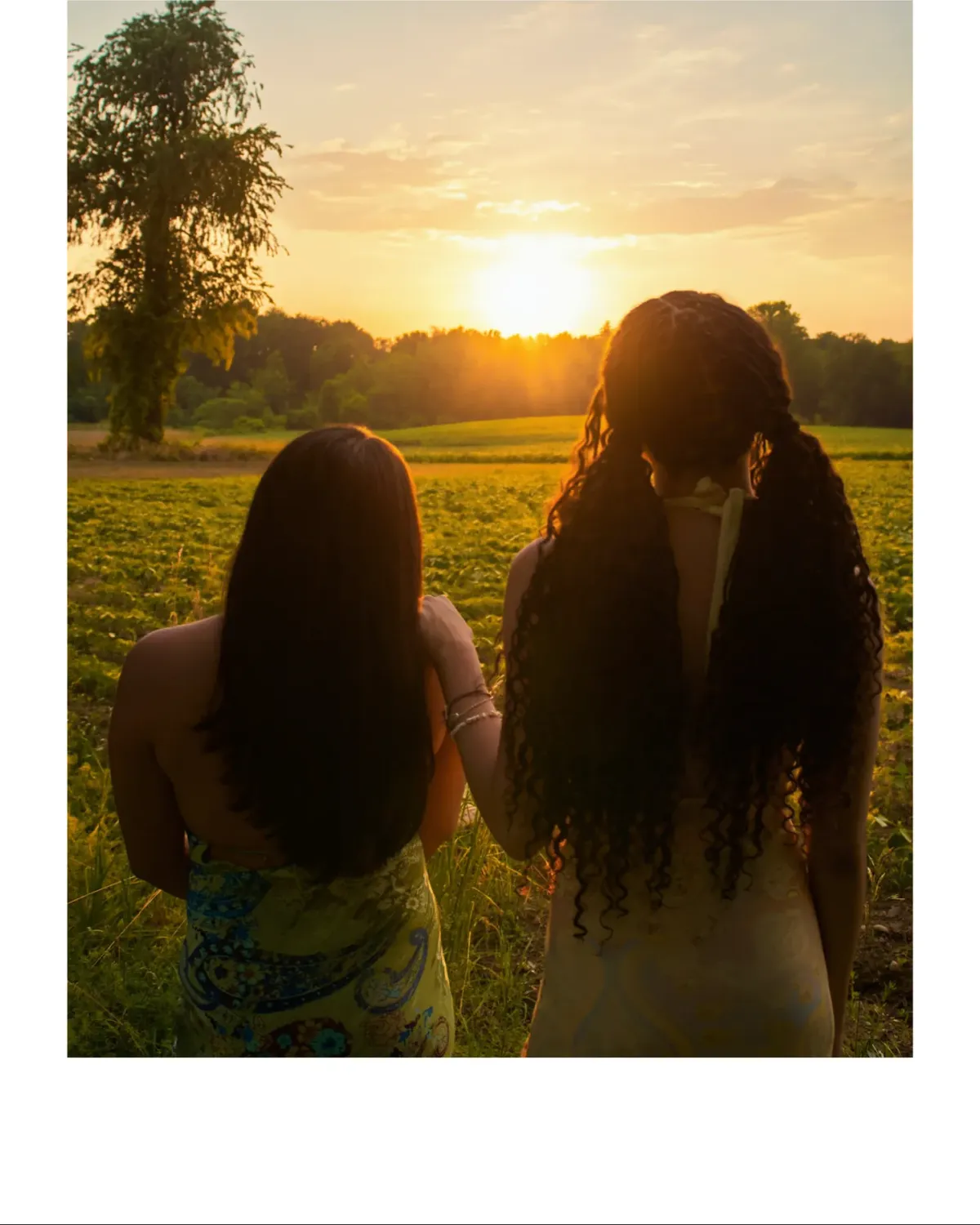 Two people standing together in a field during golden-hour sunset